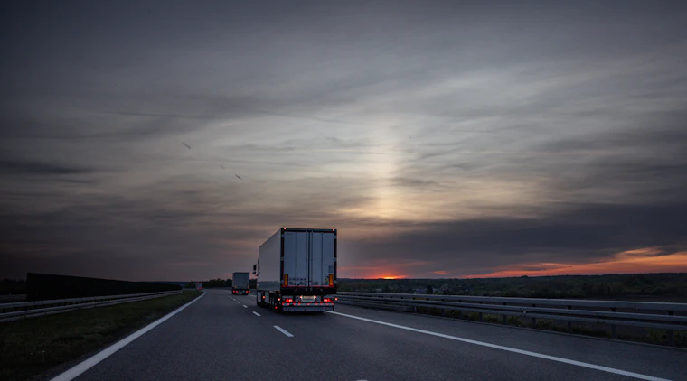 Freight trucks moving along a highway at sunset, representing coordinated transport operations