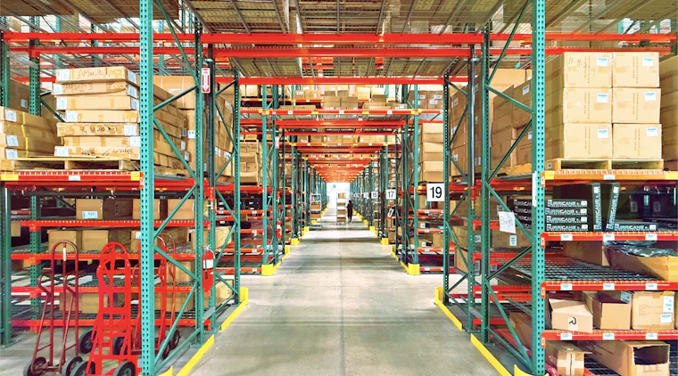Warehouse aisle stocked with shelved materials, representing procurement and supply operations
